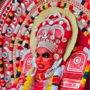 A vibrant Theyyam performer in full elaborate costume and headgear.