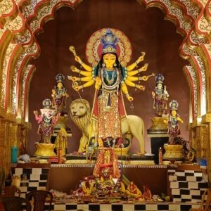 A detailed idol of the Hindu Goddess Durga with ten arms, standing on a lion and flanked by Ganesha, Lakshmi, Saraswati, and Kartikeya in an ornate setting.