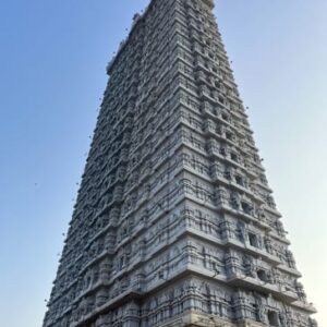 A towering grey Hindu temple gopuram with intricate carvings against a clear blue sky.