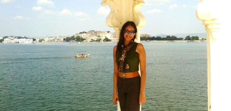 A woman stands under a decorative white archway overlooking Lake Pichola in Udaipur, India.