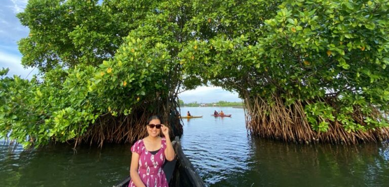 A woman in a pink dress sitting on a boat passing through a natural arch formed by lush green mangrove trees over calm water.