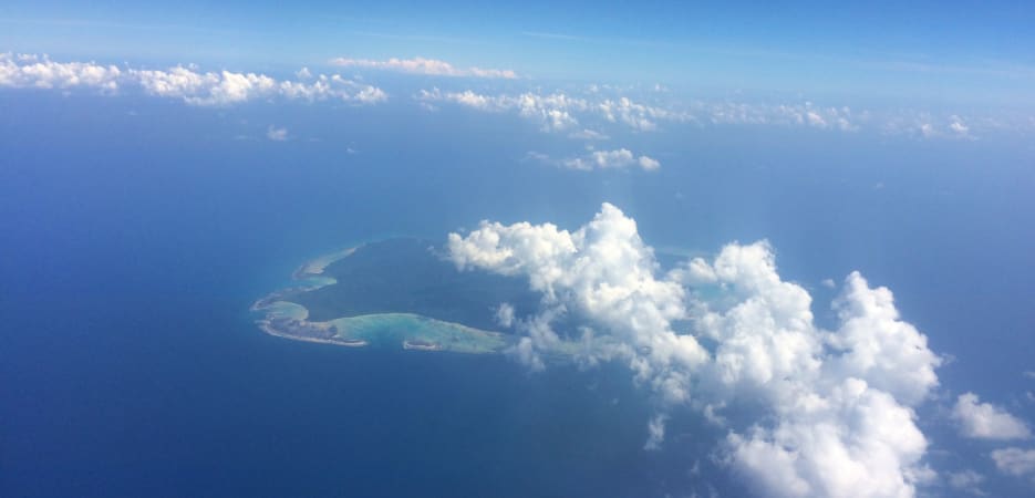 Fear while travelling - An aerial view of a green tropical island in a deep blue ocean with white clouds floating above and around it.