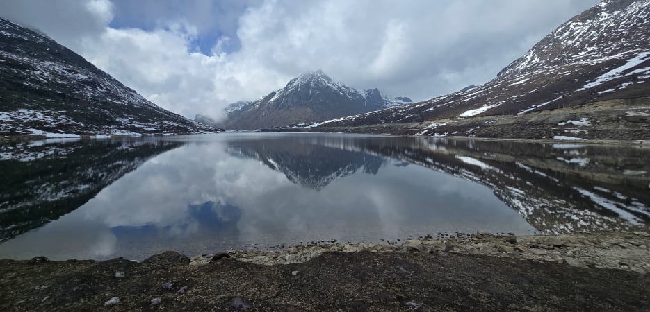 Health advisory for high altitude travel -A serene high-altitude lake reflecting snow-covered mountain peaks under a cloudy sky.