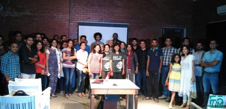 A large group of people posing for a group photo in front of a projector screen and brick wall.