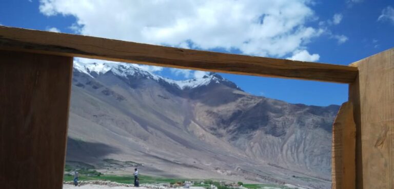 A breathtaking view of snow-capped mountains and a green valley seen through a rustic wooden frame.