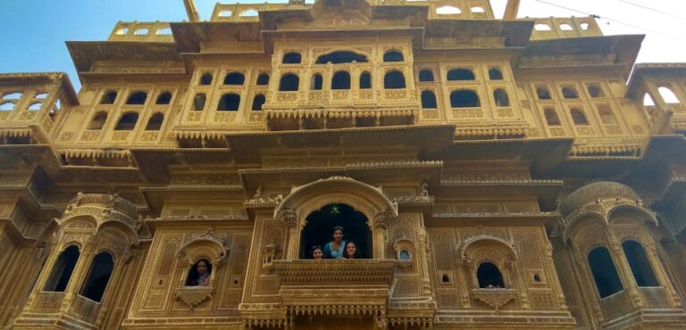 Ornate yellow sandstone facade of Patwon Ki Haveli in Jaisalmer with people looking out from the balconies.