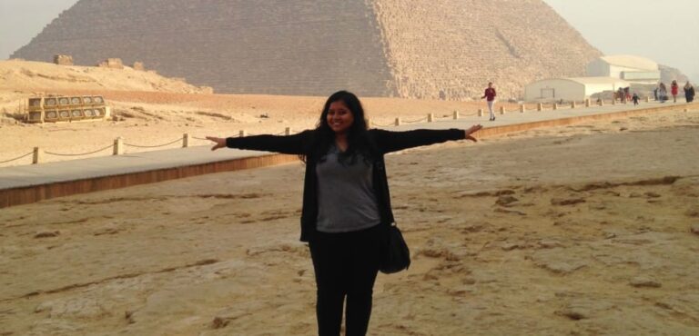 A woman stands with arms wide in front of the Great Pyramid of Giza.