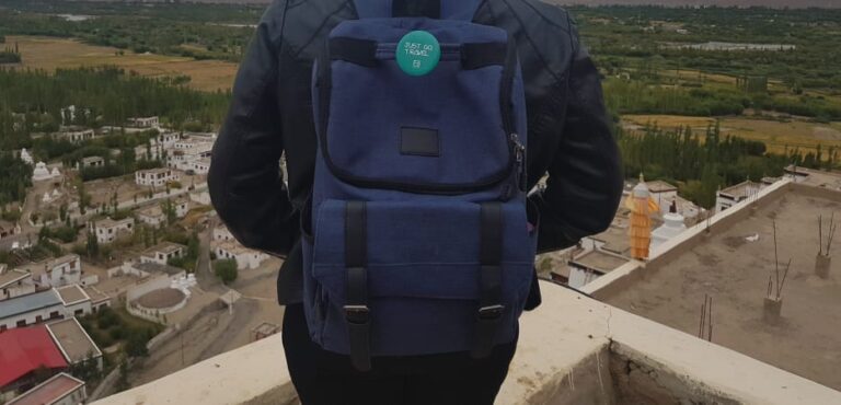 A person from behind wearing a blue backpack looking out over a vast mountain valley with a small village below.