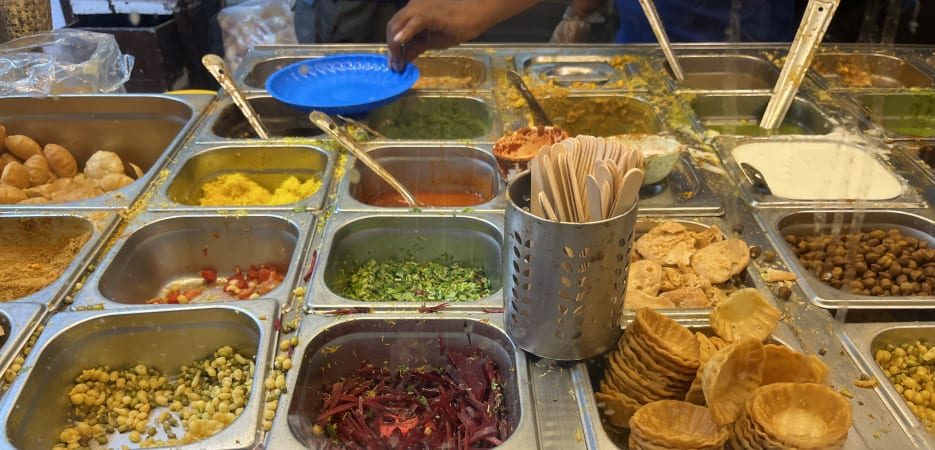 A variety of colorful ingredients for Indian chaat arranged in stainless steel containers at a street food stall.