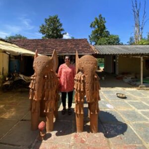 A woman stands between two large, intricately carved terracotta elephant statues in an outdoor courtyard.