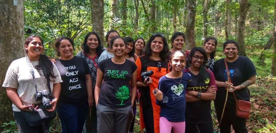 A group of smiling young women posing together in a lush green forest.