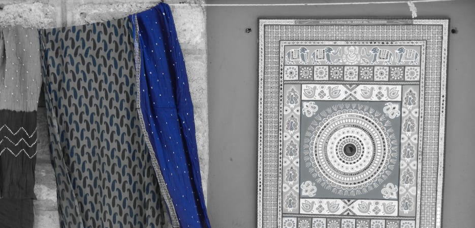 A vibrant blue cloth hangs beside a framed piece of traditional Indian artwork on a textured wall.