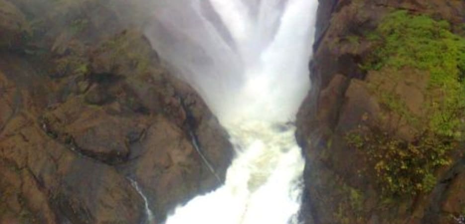 A massive white waterfall cascading down dark, wet rocky cliffs shrouded in thick mountain fog.