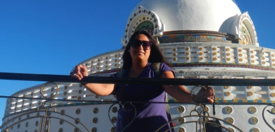 A woman poses in front of the white Shanti Stupa under a clear blue sky in Leh, Ladakh.