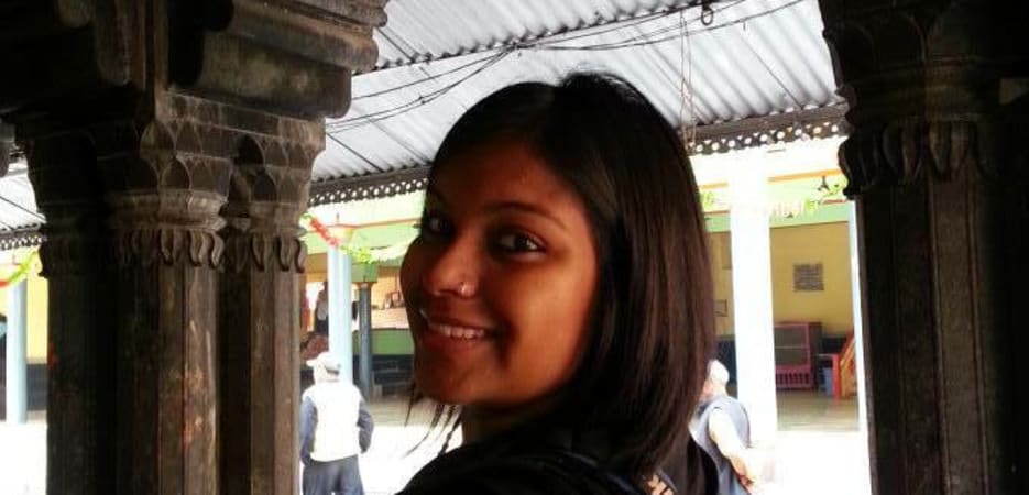 A smiling woman in a black top standing between dark carved wooden pillars at a temple.