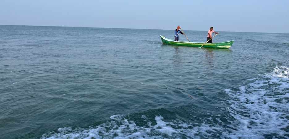 Two fishermen rowing a bright green boat on a vast, calm ocean under a clear blue sky.