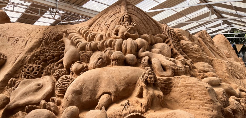 A large and detailed sand sculpture featuring Neptune, a mermaid, and various marine animals like dolphins and octopuses.