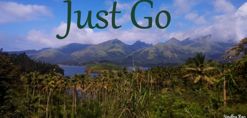 Scenic mountain range and lake view with palm trees and a blue sky with the text Just Go.