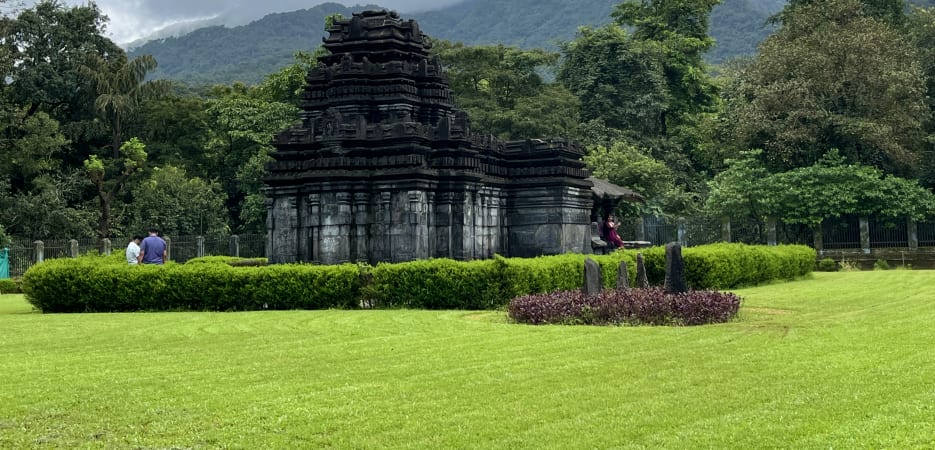 Ancient black stone Mahadev Temple at Tambdi Surla in Goa set against misty mountains.