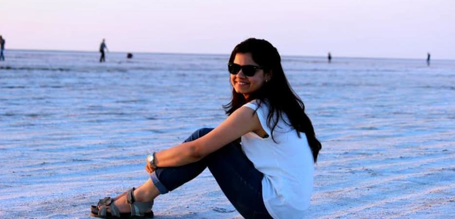 A smiling woman in a white top and jeans sitting on the white crust of a salt desert at dusk.